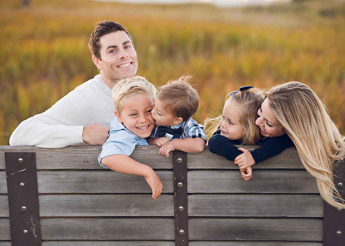 Happy family leaning on a wooden fence during a portrait session by Alicia Cervenka Photography